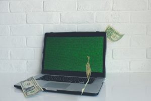 Notebook com tela verde e notas de dólar.