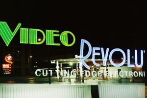 Letreiros neon em posto de gasolina à noite.